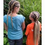 Woman and girl with blonde double Dutch braids standing in a green garden