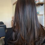 Long dark brown hair with caramel balayage highlights and curled ends in salon.