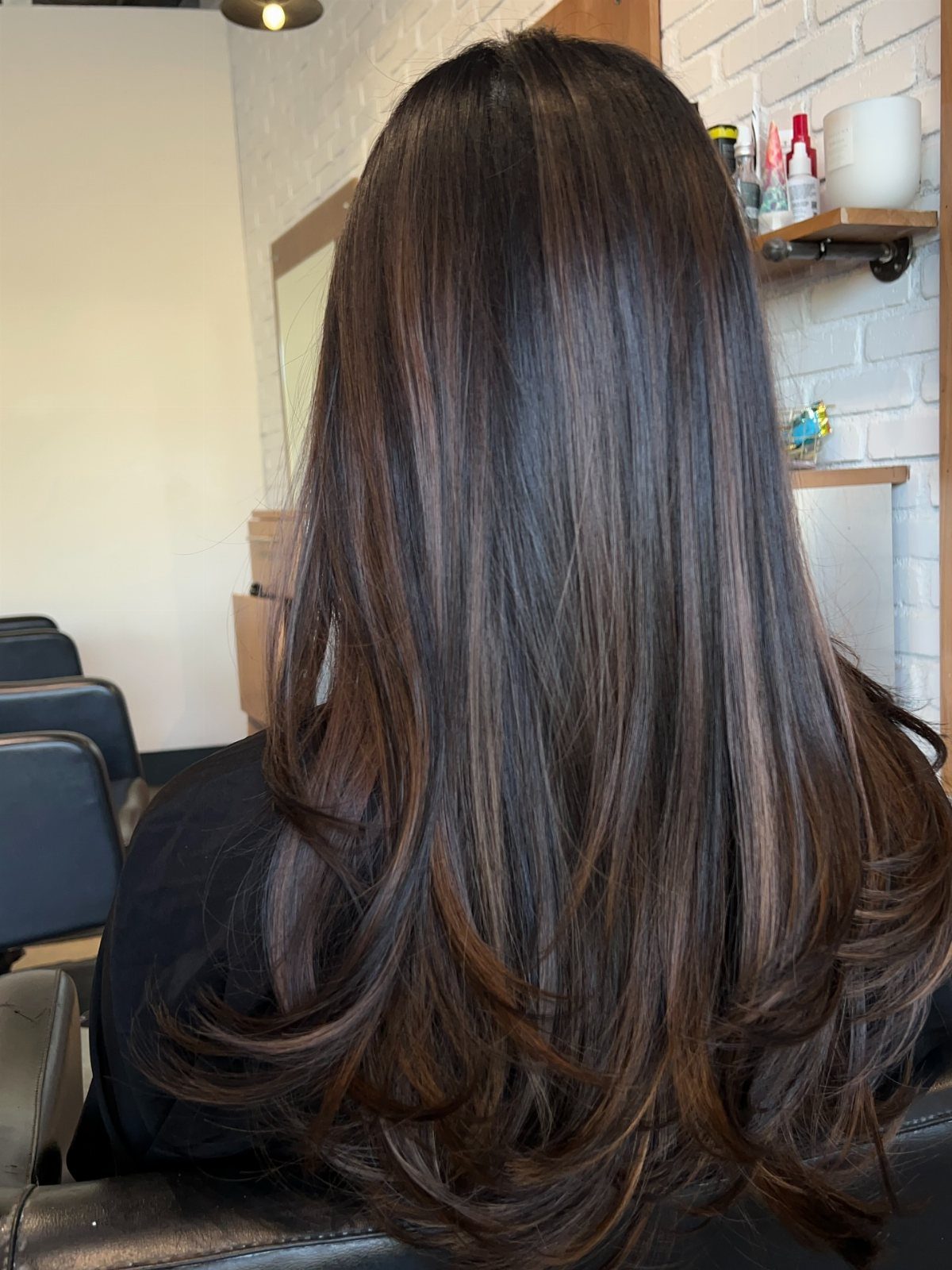 Long dark brown hair with caramel balayage highlights and curled ends in salon.